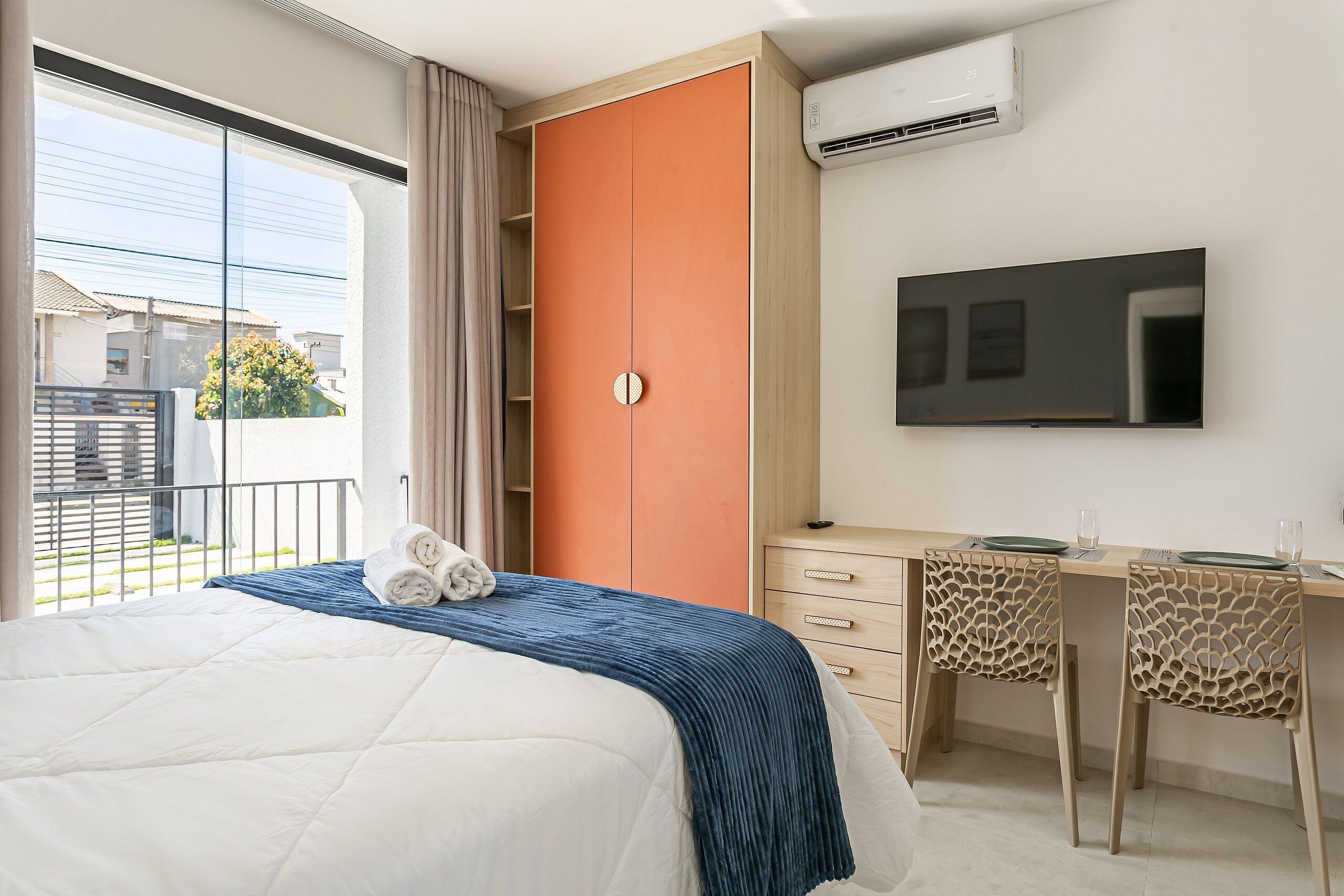 A hotel room with a bed, a desk, a television, and an air conditioning unit.