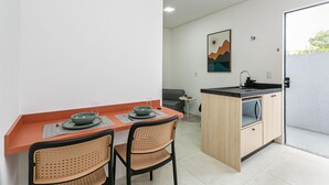 A compact kitchen with a dining area, featuring a small island, two chairs, and a dining table with a bowl and glass.