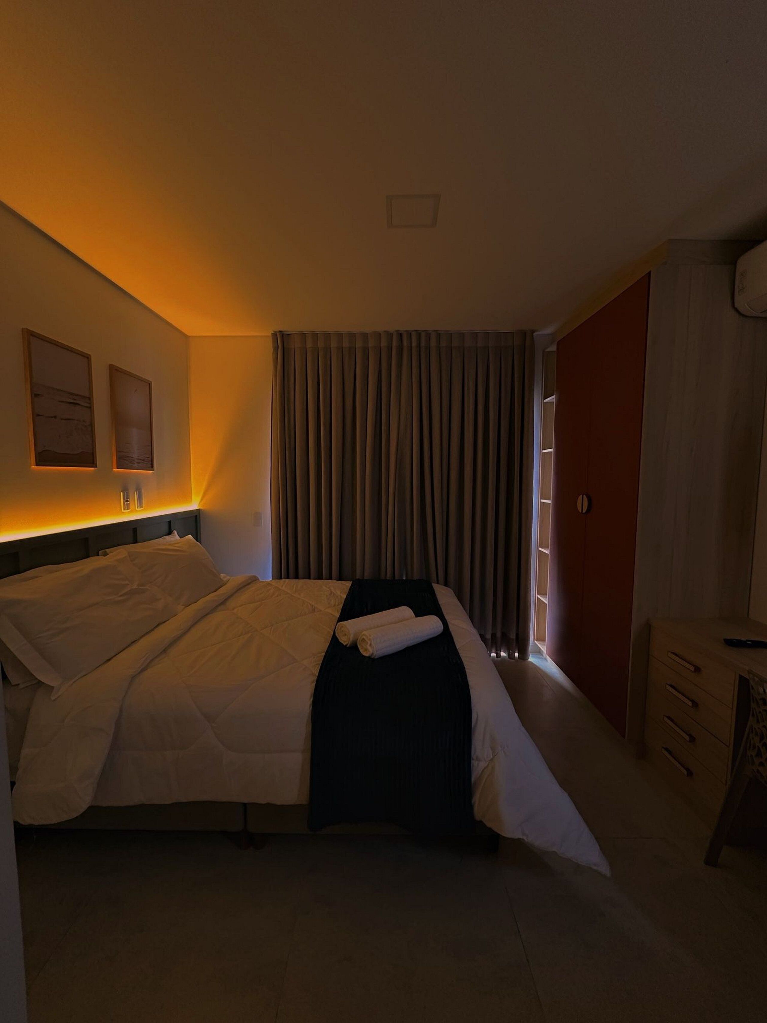 Une chambre d’hôtel avec un lit, une table de chevet, une armoire et une fenêtre avec des rideaux.