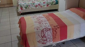 Un dormitorio con dos camas, una con cubrecama floral y la otra con cubrecama a rayas. Hay un armario y una pequeña mesa con una silla.
