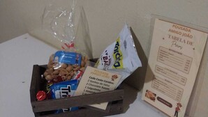 Una caja de madera llena de diversos aperitivos y un menú sobre una mesa, frente a una pared lisa.