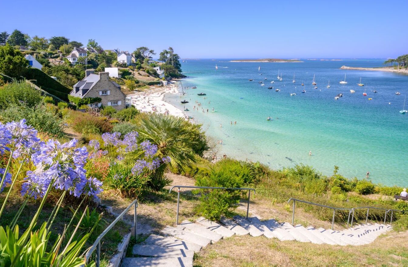 Un pueblo costero con playa, aguas cristalinas y barcos.