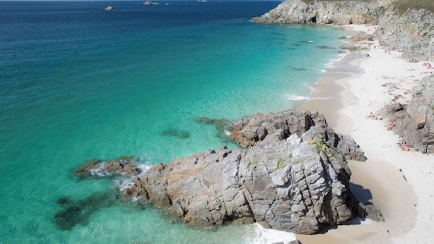Een kuststrand met helder turquoise water, rotsformaties en een zandrijk strand.