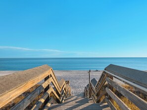 A wooden boardwalk leading to a beach with a clear blue sky.