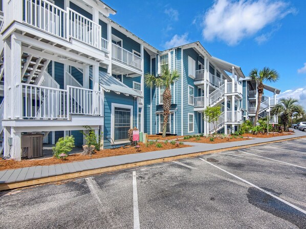 A beachfront building with multiple balconies, a parking lot, and a clear sky.
