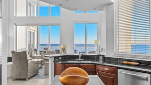 Una cocina moderna con un recipiente de madera grande como elemento central, encimera negra y vistas al océano a través de amplios ventanales.