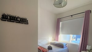 A bedroom with a bed, a small table, a window with curtains, and a wall decoration.