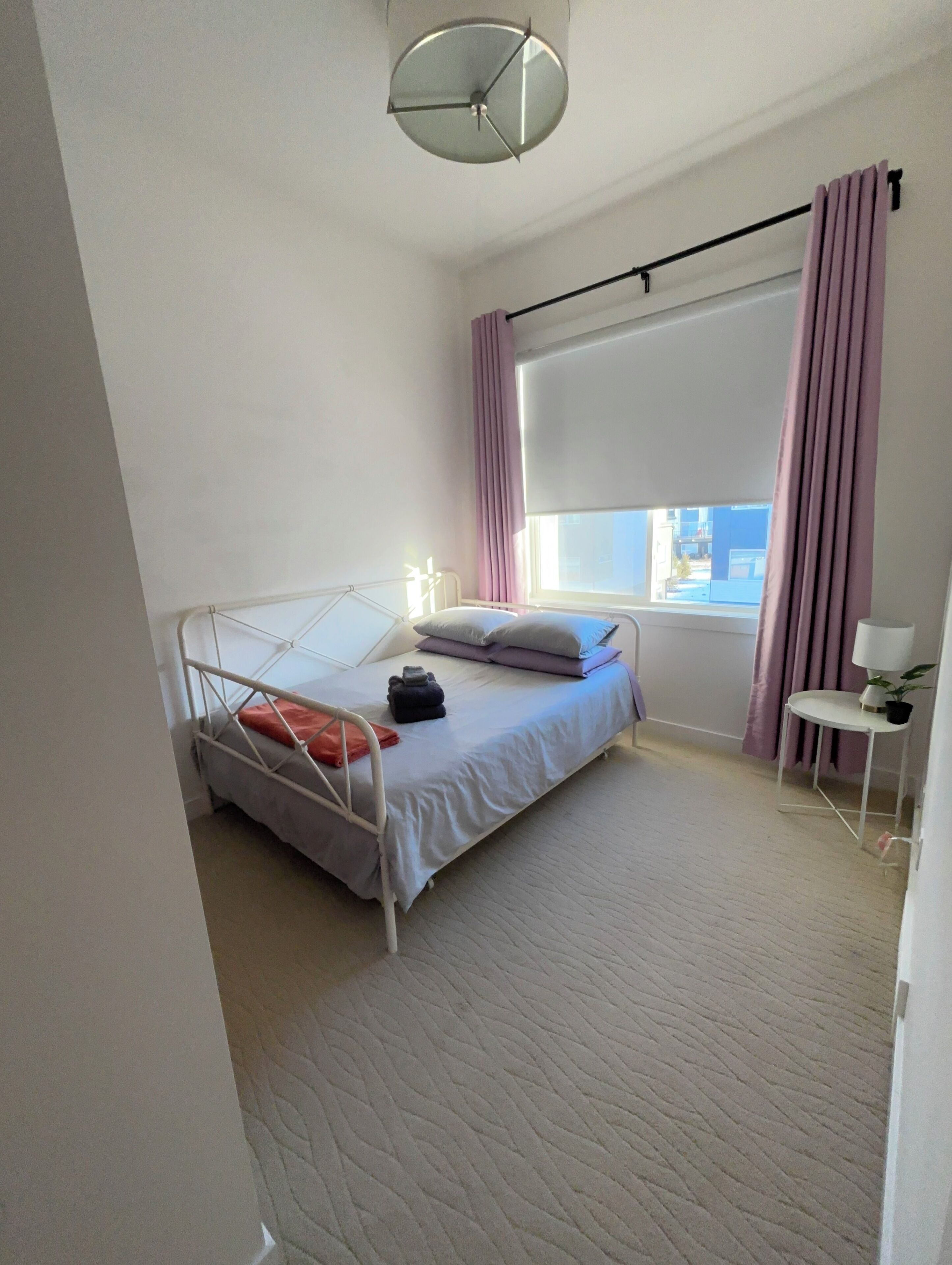 Un dormitorio con una cama individual, una ventana con cortinas, una mesita de noche con lámpara y vistas al exterior.