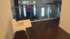 A spacious living area with a high ceiling, a staircase, and a glass railing.