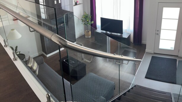 A modern apartment with a glass staircase, a living area with a sofa, a TV, and a potted plant.