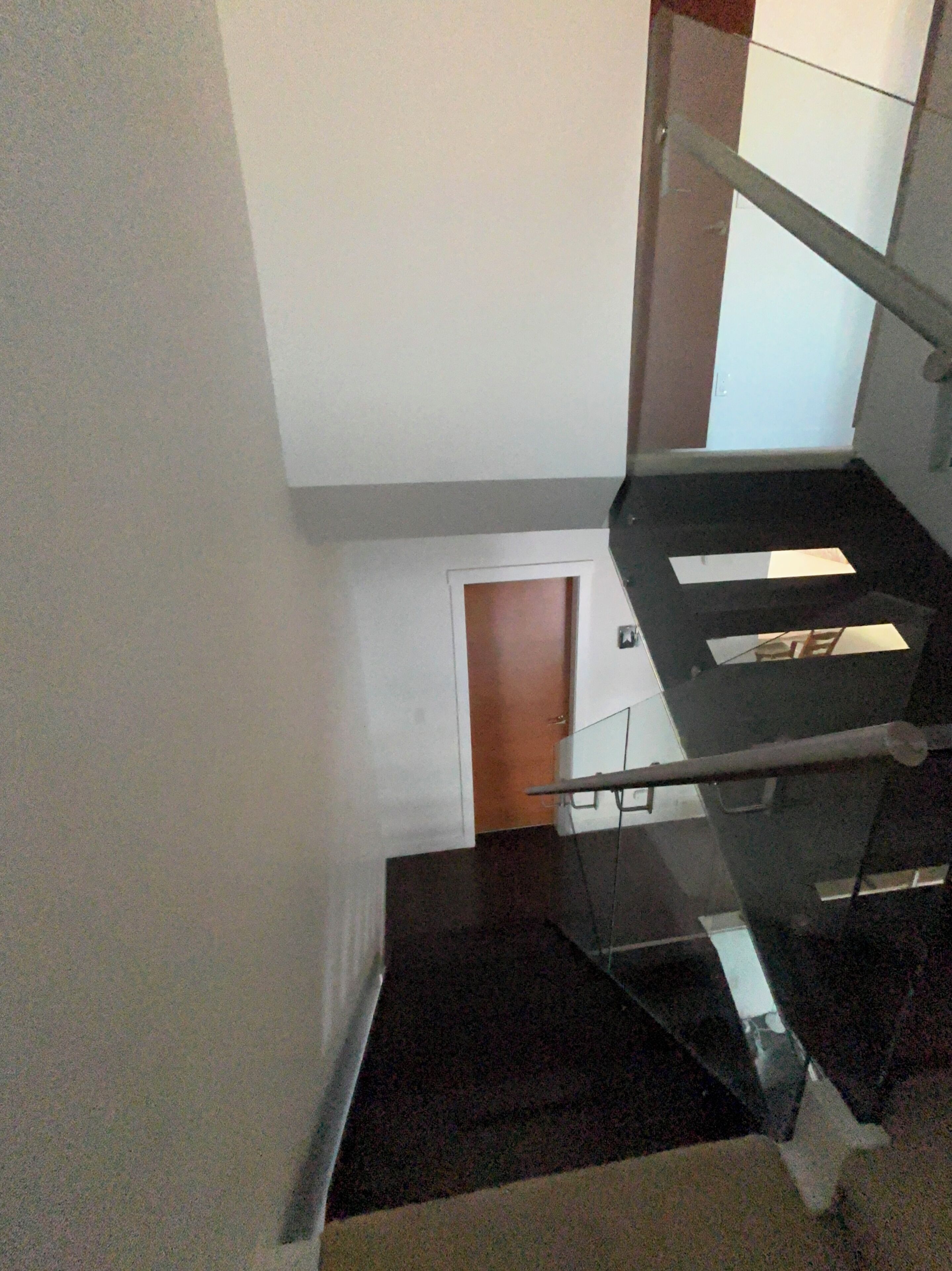 A staircase with a glass railing, a door at the bottom, and a white wall.