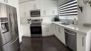 A modern kitchen with stainless steel appliances, white cabinetry, and a dark wood floor.