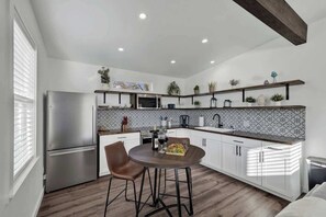 A modern kitchen with white cabinets, a stainless steel refrigerator, and a dining area with two chairs. - Evergreen Escape: Hot-Tub,5 Min Downtown! (Fredericksburg)