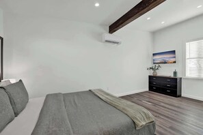 A bedroom with a bed, a dresser, a window with blinds, and an air conditioning unit.
