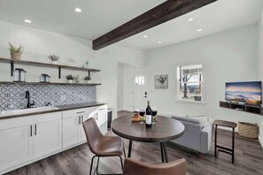 Una cocina moderna con armarios blancos, un salpicadero estampado y un rincón de comedor con una mesa redonda y sillas.