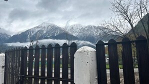 A wooden fence with a metal gate, a white post, and a mountainous landscape with snow-covered peaks in the background. - WATERFRONT PINE PAHALGAM (Anantnag)