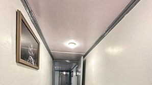 A narrow hallway with white walls, a framed picture on the left, and a light switch on the right. - WATERFRONT PINE PAHALGAM (Anantnag)