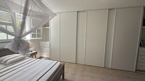 Un dormitorio con cama, mesita de noche, armario y ventana con vistas a zonas verdes.