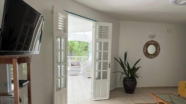 Un salón con televisor sobre un mueble, una planta en maceta y una zona de comedor con una silla.