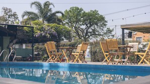 A swimming pool with wooden lounge chairs and a covered seating area. - Hostel Pura Vida Mae (Yerba Buena)