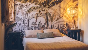 A bedroom with a bed, pillows, a nightstand, a lamp, and a wall mural. - Hostel Pura Vida Mae (Yerba Buena)