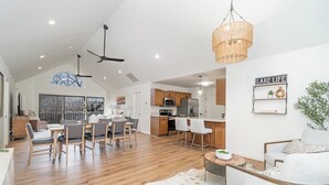 A spacious living area with a dining table, chairs, a kitchen with wooden cabinets, and a large window offering a view. - Lake Point Escape - Dock and Hottub on Belews Lake (Forsyth County)