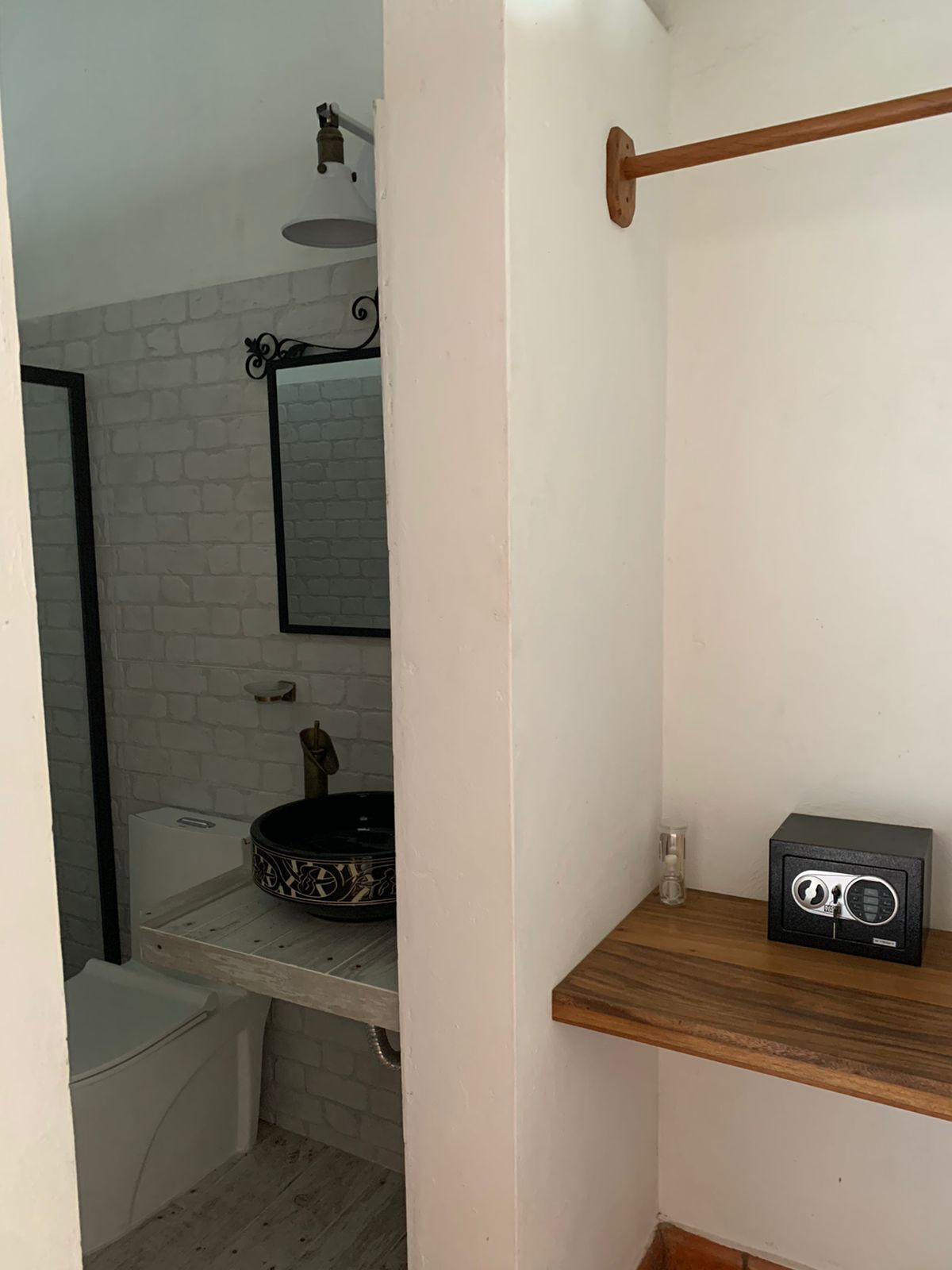 A bathroom with a white brick wall, a black-framed mirror, a wooden shelf, and a black radio.