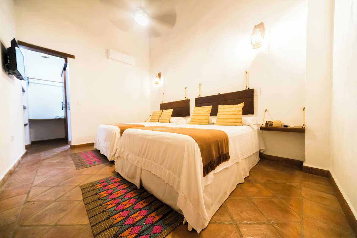 A hotel room with two beds, a small bedside table, a TV mounted on the wall, and a door leading to a hallway.