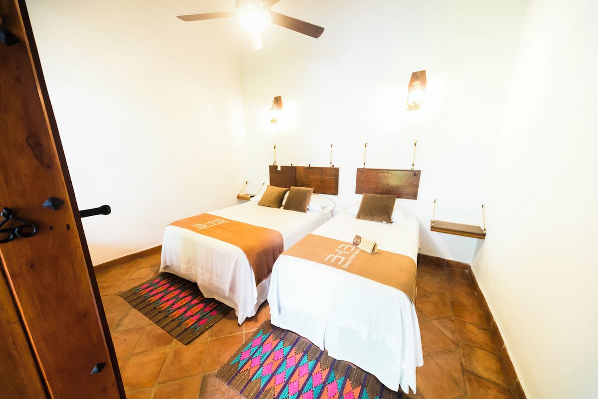 A hotel room with two beds, a ceiling fan, and a small shelf.