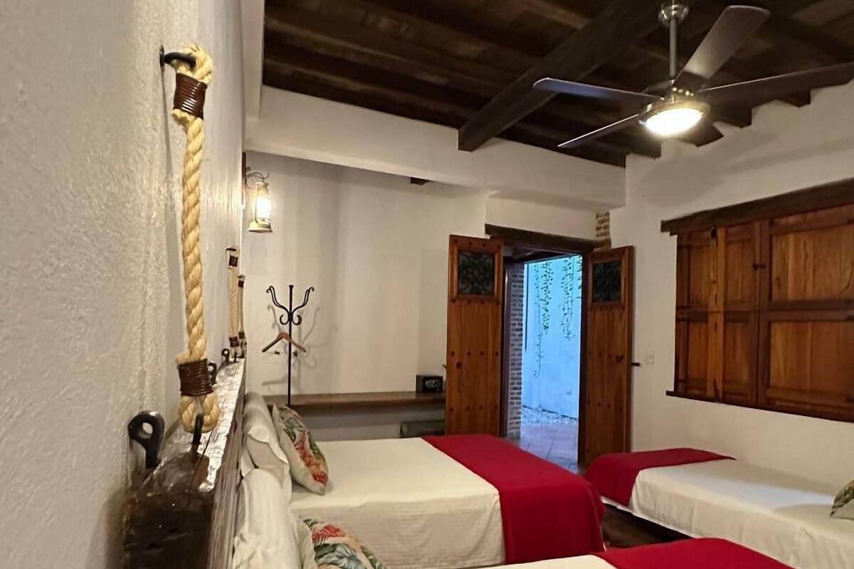 A room with two beds, wooden beams on the ceiling, a ceiling fan, and a window with a view.