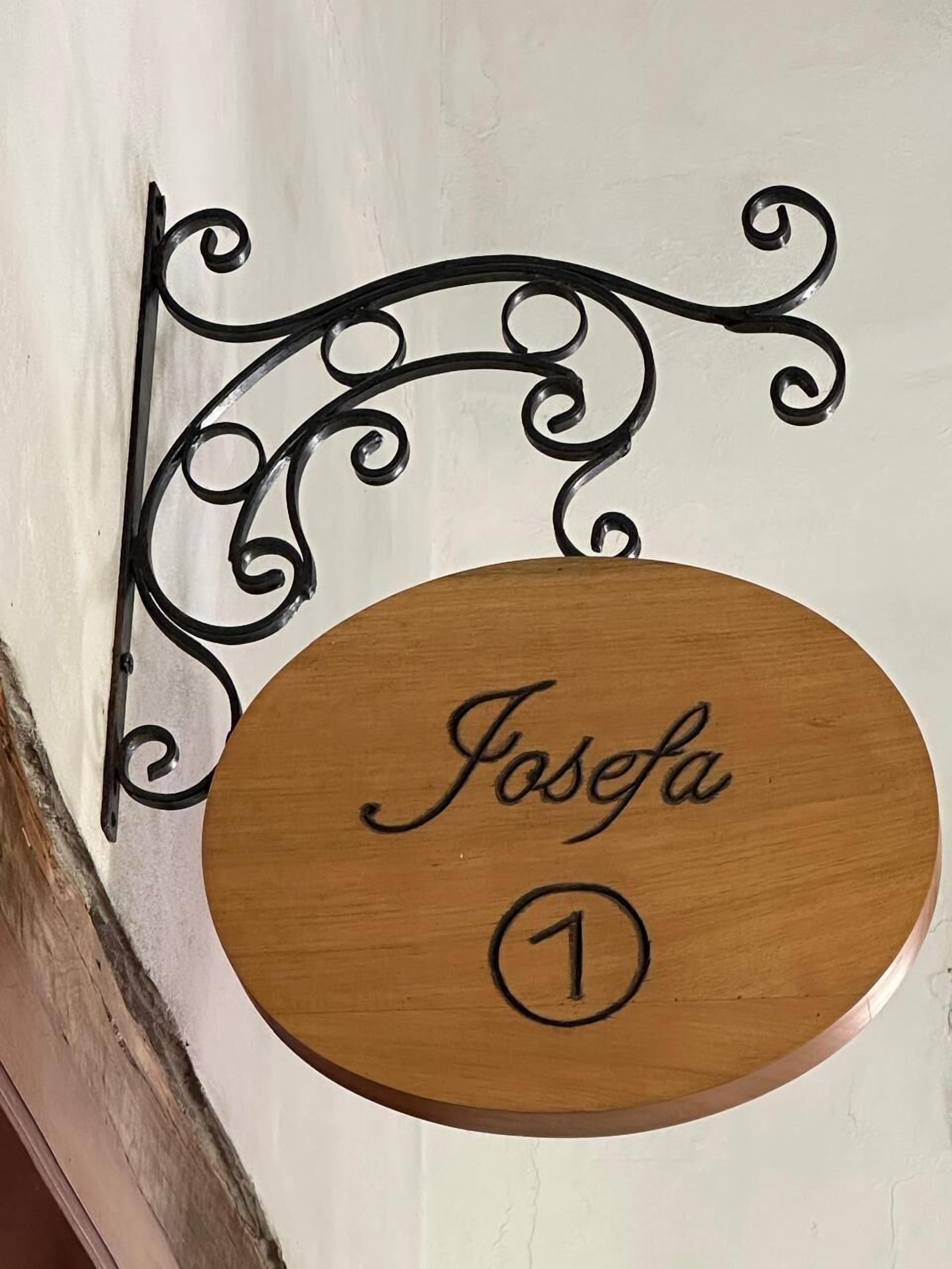 Een houten plaquette met de naam 'Josefa' en het nummer '1', bevestigd aan een muur met een decoratieve metalen beugel.