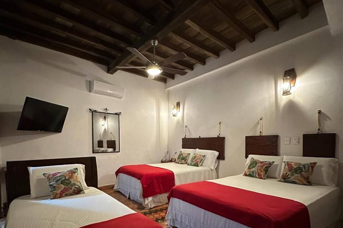 A hotel room with three beds, a TV, a mirror, and a ceiling fan.
