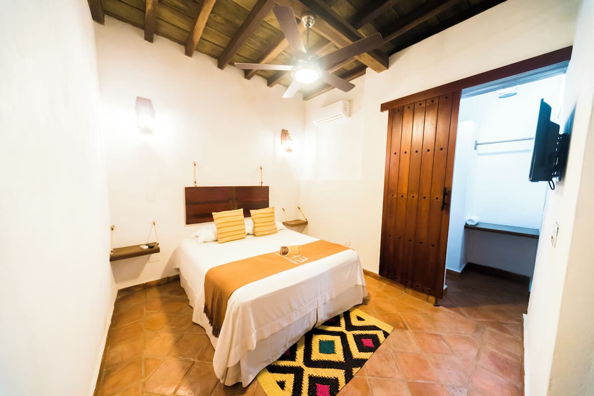 A bedroom with a bed, a ceiling fan, a wooden door, and a TV mounted on the wall.
