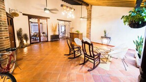A spacious room with a tiled floor, wooden ceiling beams, rocking chairs, a bicycle, and hanging plants. - BOHEMIA HOTEL BOUTIQUE  (Mompos)