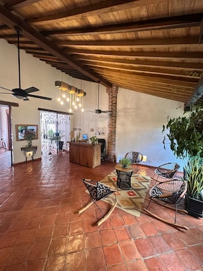 A spacious indoor area with a high ceiling, wooden beams, and a tiled floor. There are several chairs and a table, a reception desk, and a large window with decorative ironwork. - BOHEMIA HOTEL BOUTIQUE  (Mompos)