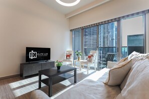 A modern living room with a flat-screen TV, a sofa, a coffee table, and a balcony with chairs. - Stunning Lake View 1BHK Retreat in Dubai (Dubai)
