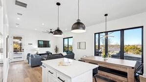Una cucina moderna con isola centrale, illuminazione a sospensione e ampie finestre che offrono vista sull'esterno.