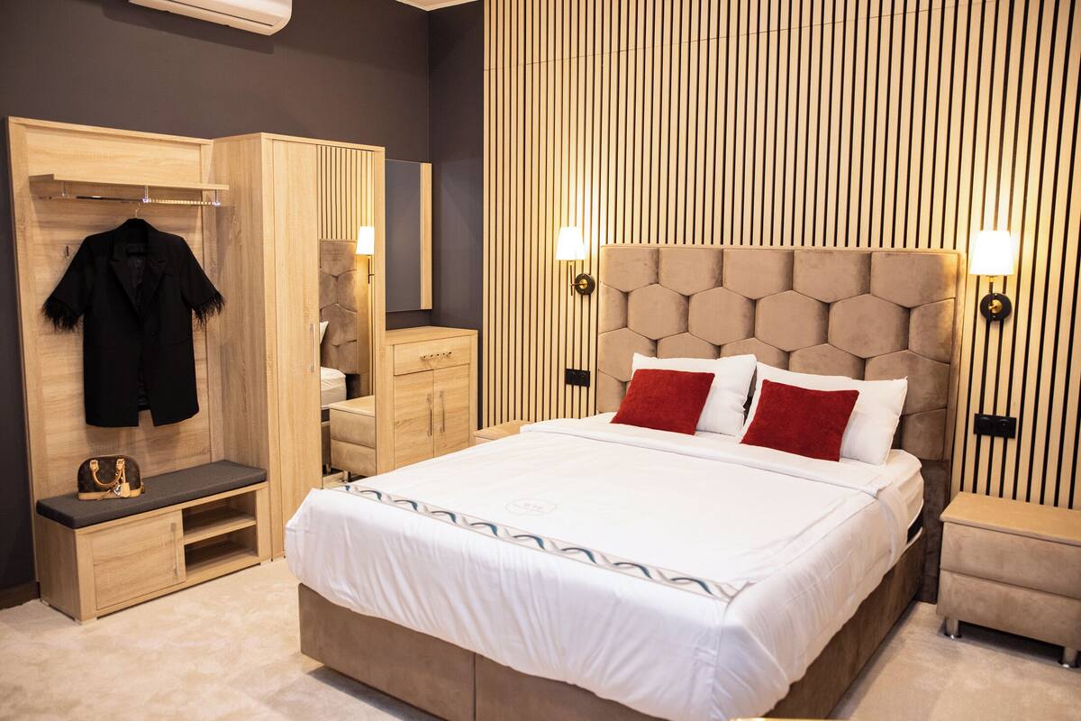 Un dormitorio moderno con una cama grande, un armario de madera, un banco y una mesita de noche.