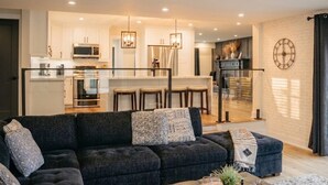 Ein modernes Wohnzimmer mit einer dunklen Couch, einem Couchtisch und einer Küche im Hintergrund.