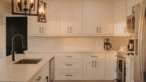 Eine moderne Küche mit weißen Schränken, einer Marmorarbeitsplatte, einem eingebauten Backofen und einem Edelstahl-Kühlschrank.