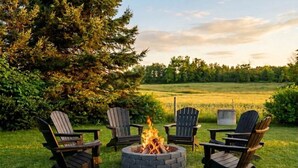 Ein Feuerkorb mit vier Adirondack-Stühlen, die ringsherum in einer grünen Außenanlage angeordnet sind.