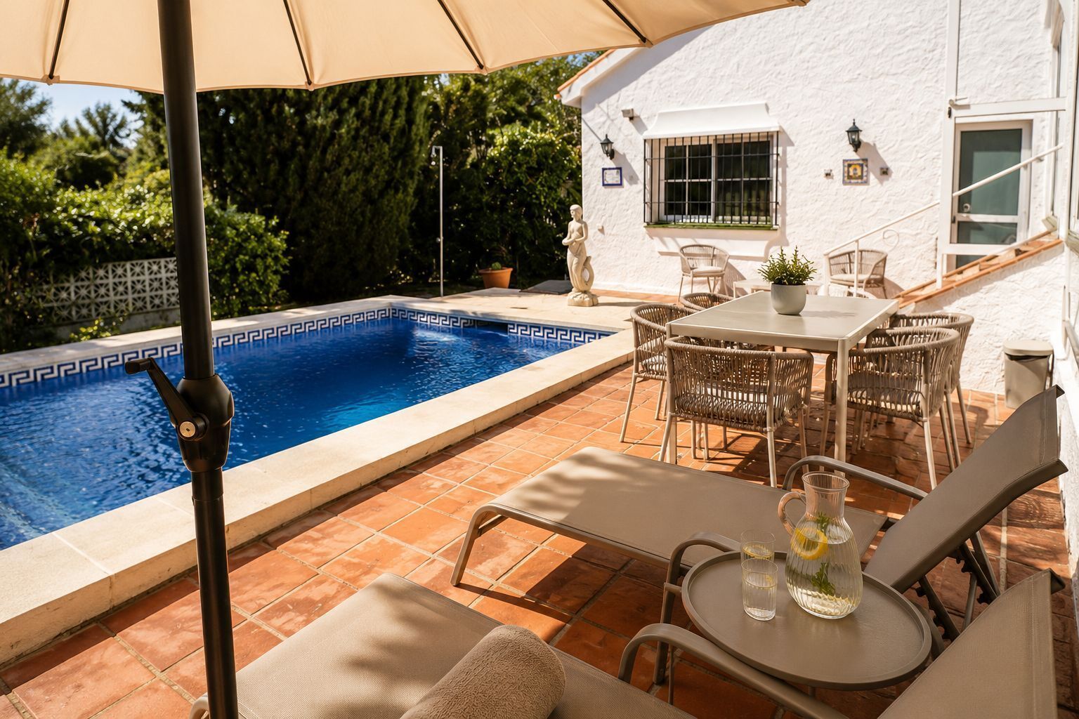 A poolside area with a pool, outdoor furniture, and a white building in the background.
