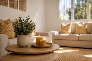 Een woonkamer met een ronde houten tafel, een potplant en twee brandende kaarsen.