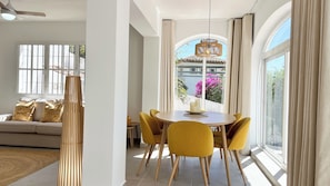 A dining area with a round table, yellow chairs, and a view of a building with pink flowers outside.