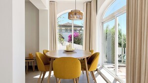 Un coin repas avec une table ronde, des chaises jaunes, un luminaire suspendu et une vue sur un immeuble et des arbres, visible à travers de grandes fenêtres.