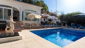Une piscine avec des chaises longues et des parasols, une statue et un espace patio.
