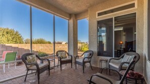 Un patio couvert, aménagé avec des meubles en osier et doté de grandes fenêtres offrant une vue sur le paysage environnant.