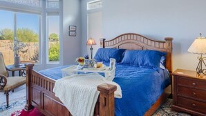 Une chambre avec un grand lit, une tête de lit en bois, une table de chevet, une lampe et une fenêtre donnant sur un paysage verdoyant.