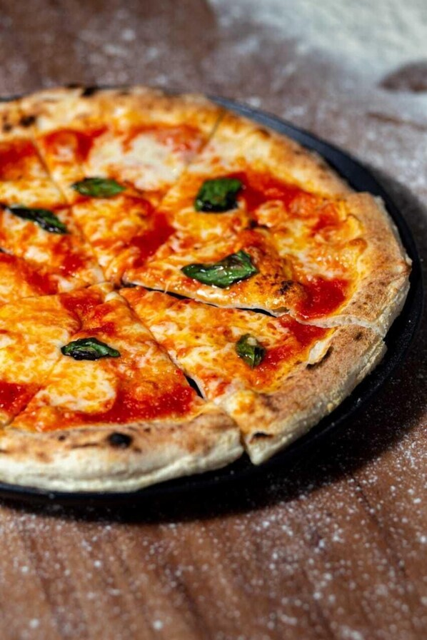 A pizza with visible toppings and a crust, placed on a dark surface. - Pousada Maple Monte Verde (Camanducaia)