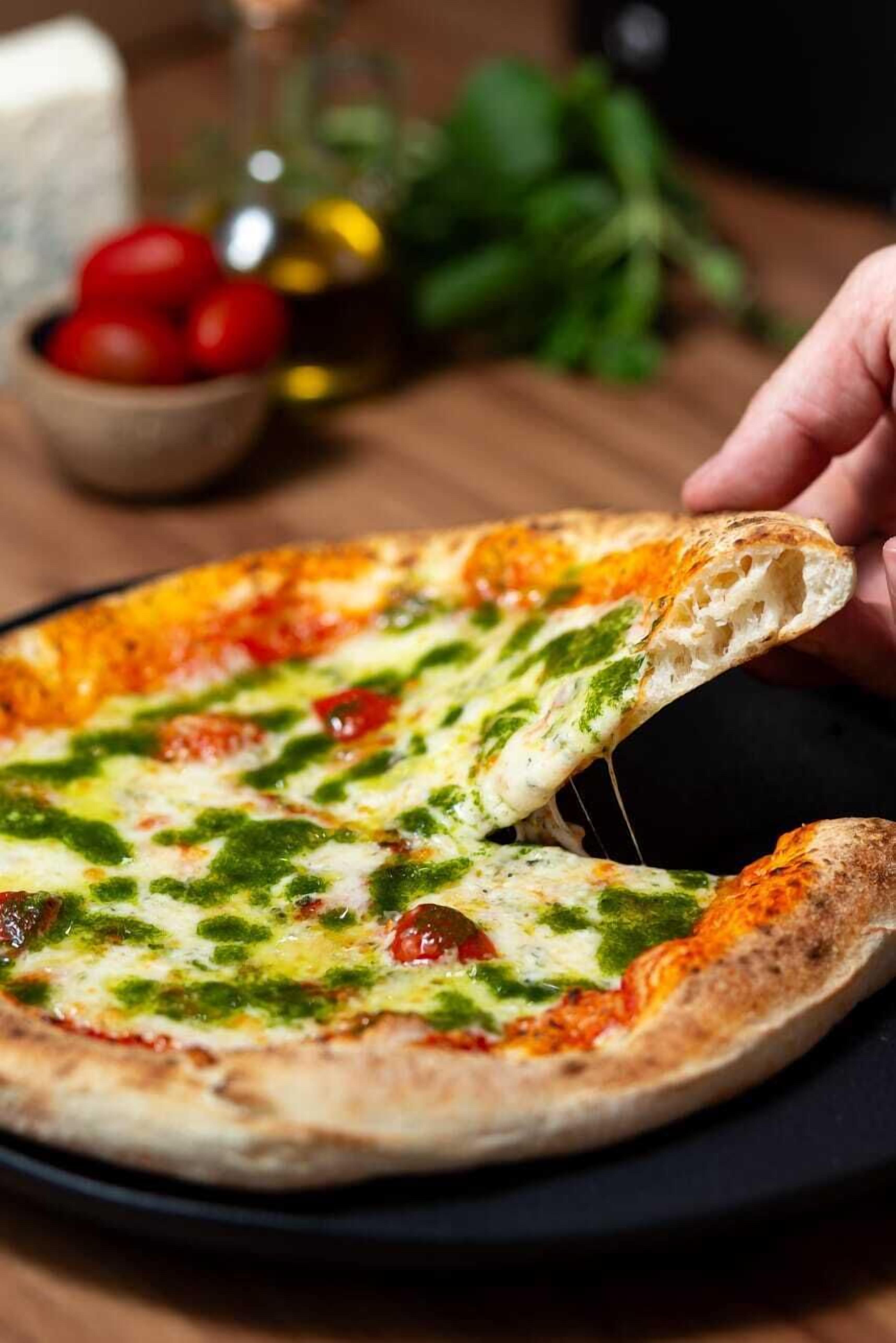 Pizza con pesto verde y tomate, sobre un plato negro.